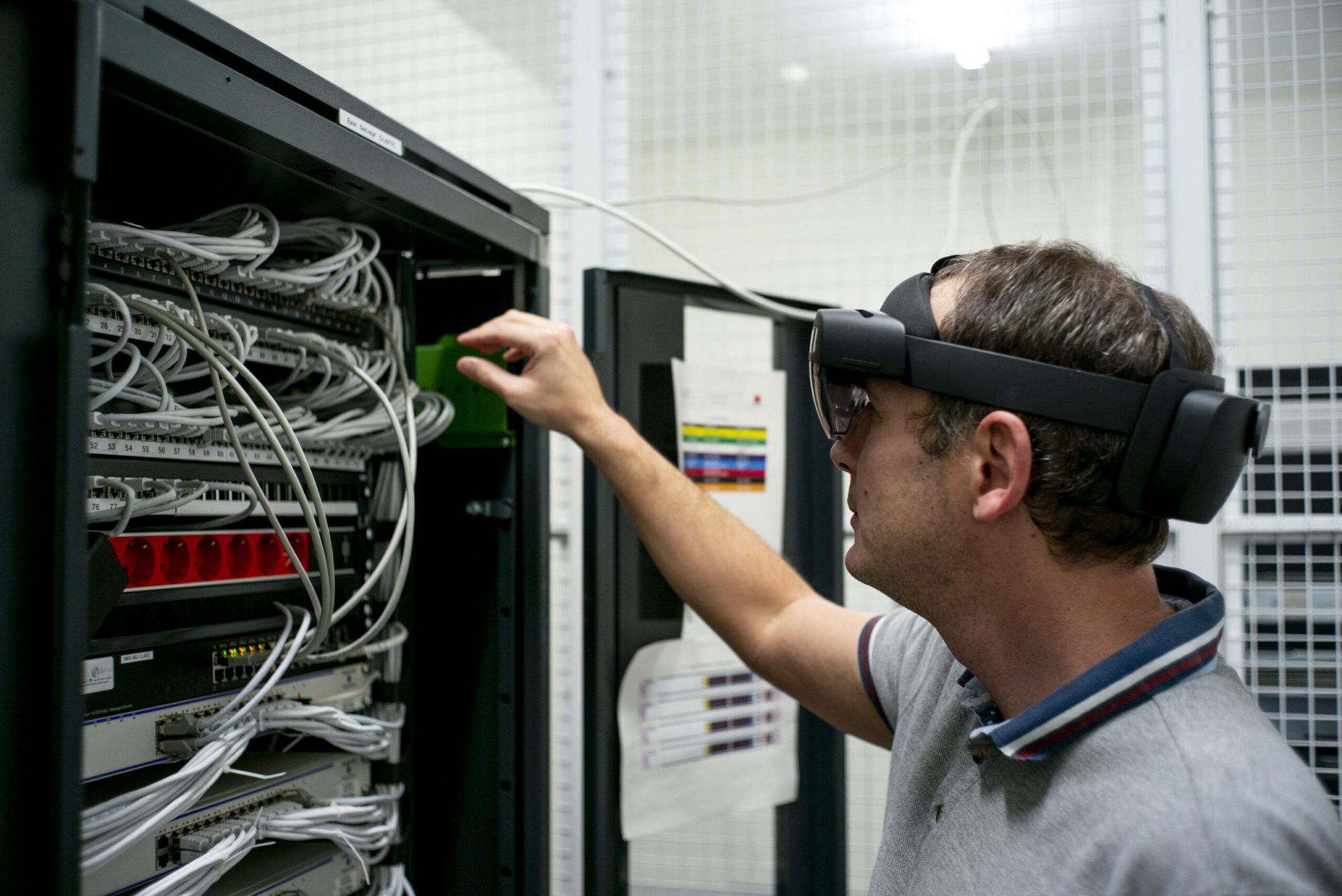 Une personne avec un casque de réalité augmentée en train de vérifier les câbles des serveurs et d'être guider par celui-ci